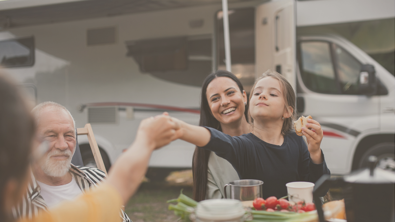 A multi-generational family eating outdoors beside their RV, enjoying an off-grid camping experience together.